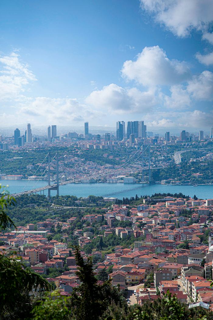Yüksek bir tepeden İstanbul: önde konut mahalleleri, ortada Boğaz Köprüsü, arkada gökdelenler