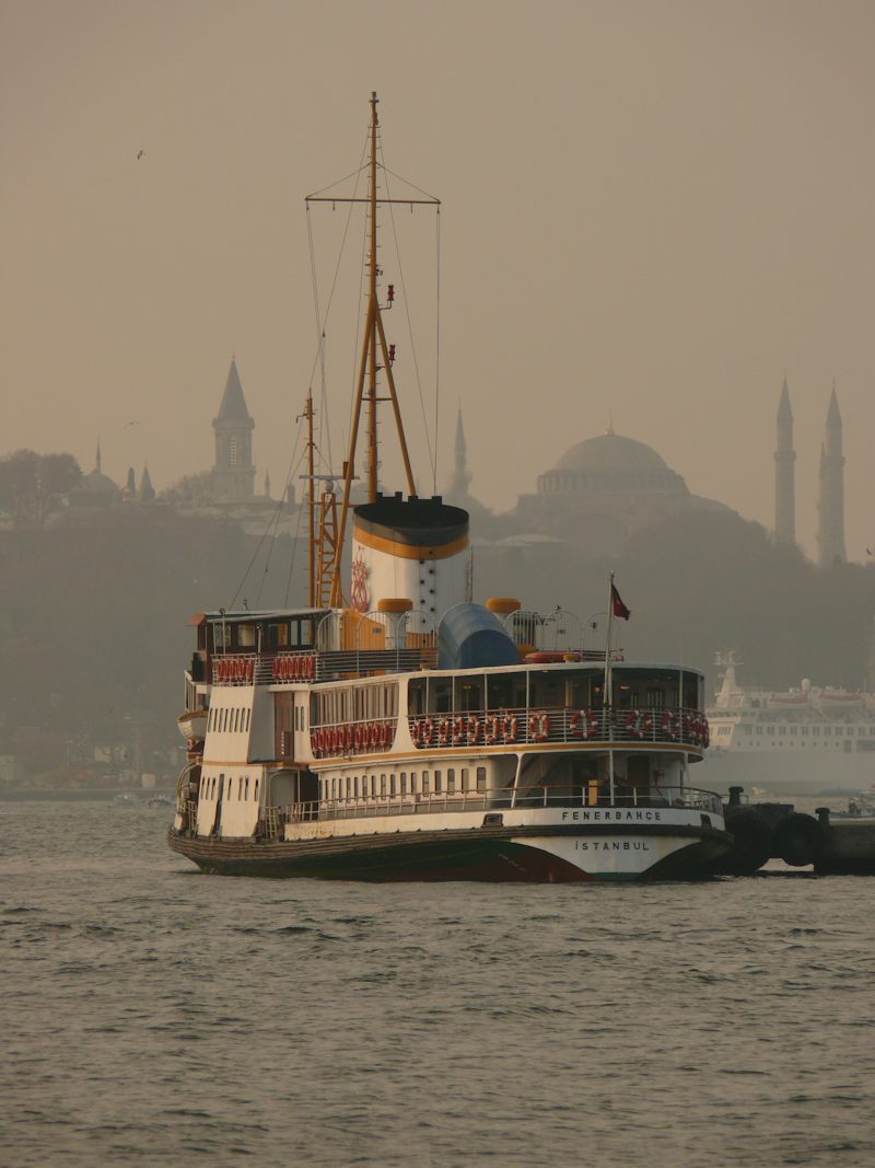 Puslu havada Boğaz'da ilerleyen klasik bir şehir hatları vapuru, arkada cami silueti